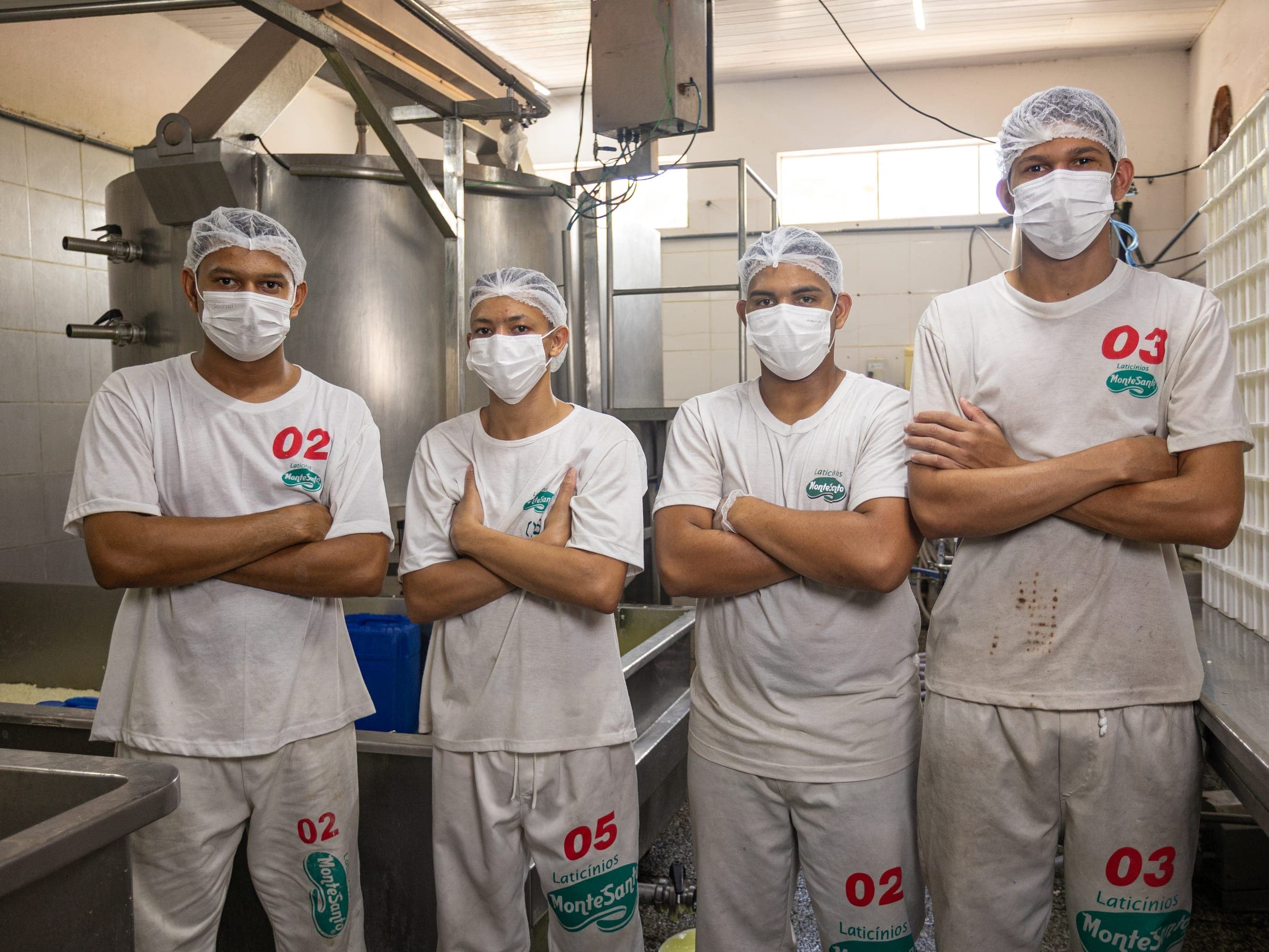 Equipe da produção de queijo, de braços cruzados, ao lado das formas