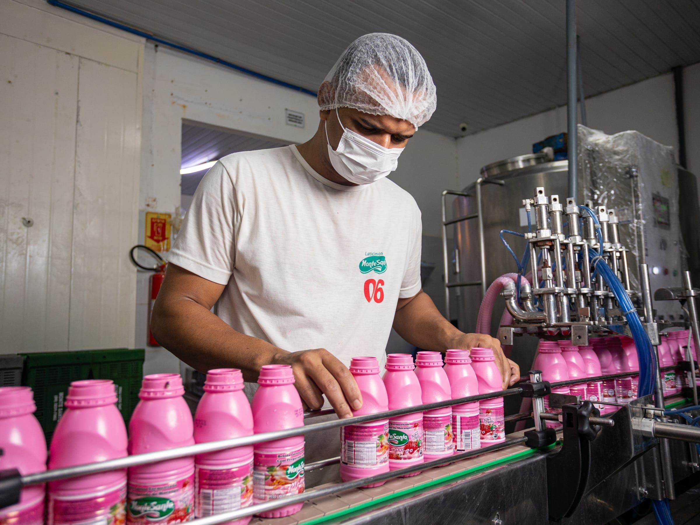 Funcionário conferindo garrafas de bebida láctea de morango na linha de envase